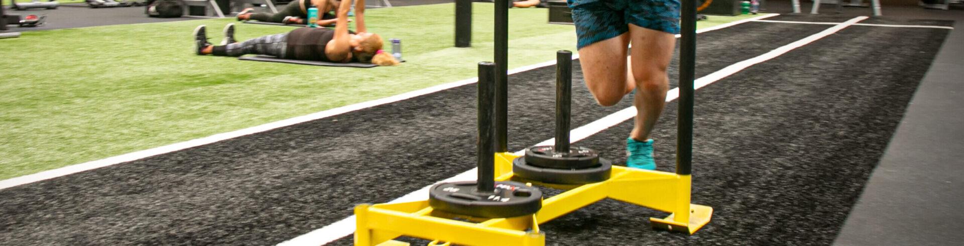 eos gym member pushing a sled on eos branded indoor turff 